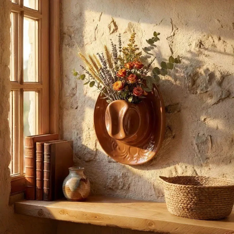 Glazed ceramic cowboy hat wall vase in brown, mounted on a wall and filled with dried flowers
