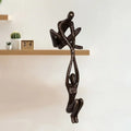 Bronze-tone resin sculpture of two abstract figures balancing together, mounted on the edge of a wooden shelf