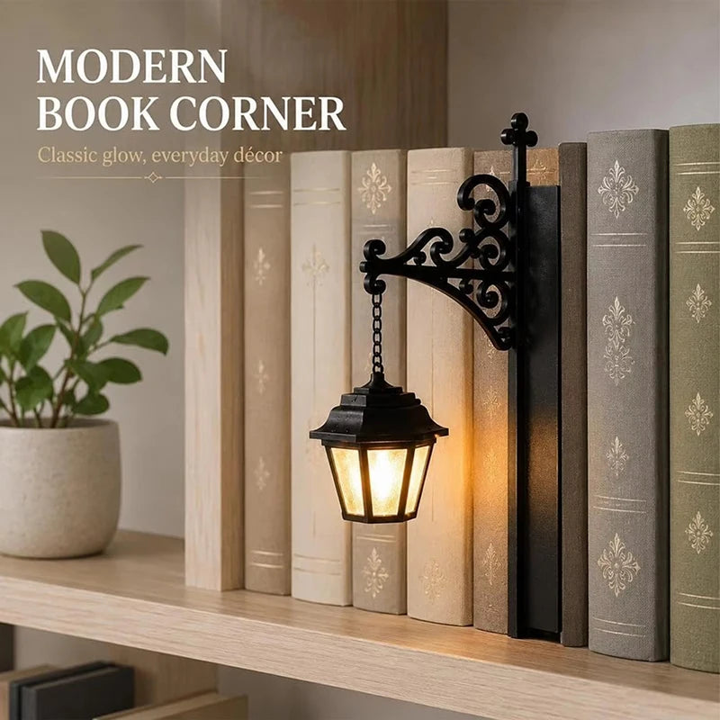 Vintage black wrought-iron style miniature street lamp with warm LED glow, displayed beside books on a shelf