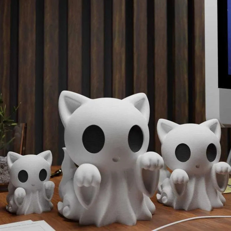 Three sizes of white ghost cat figurines lined up on a desk