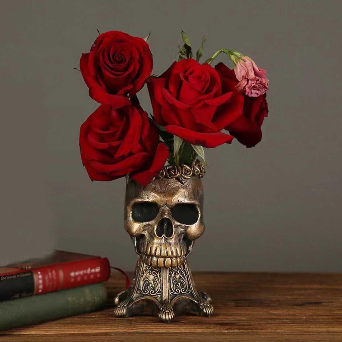 Bronze gothic skull vase with red roses on a wooden table