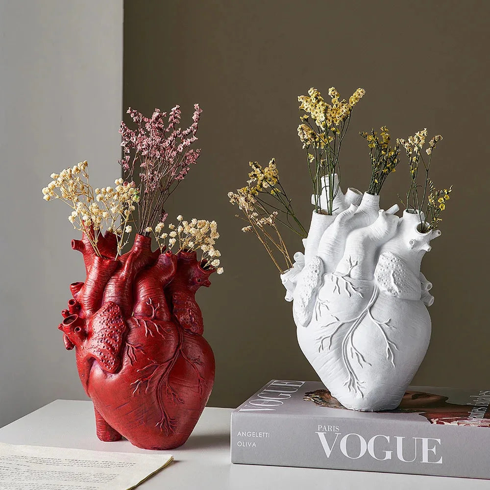 Red and white anatomical heart vases with dried flowers displayed on books