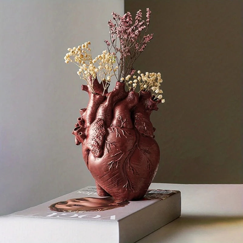 Dark red anatomical heart vase with dried flowers resting on a book