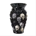 Black resin vase covered in black, silver and white skull sculptures on white background