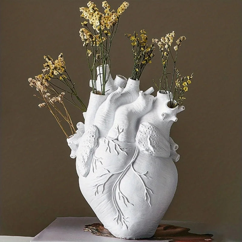 White anatomical heart-shaped vase with dried yellow flowers on a pedestal