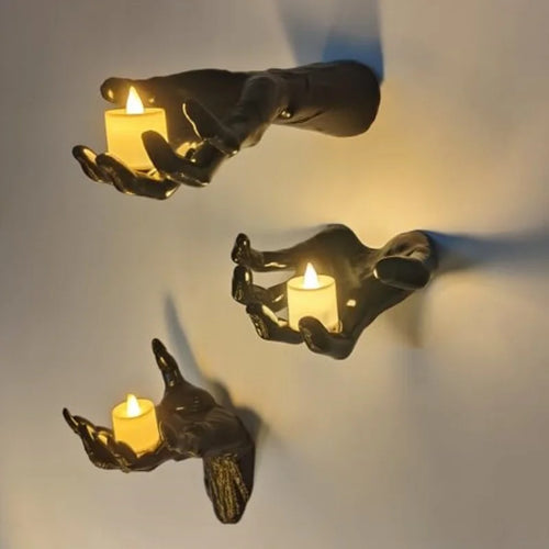 Three black wall-mounted hands cupping flickering LED candles