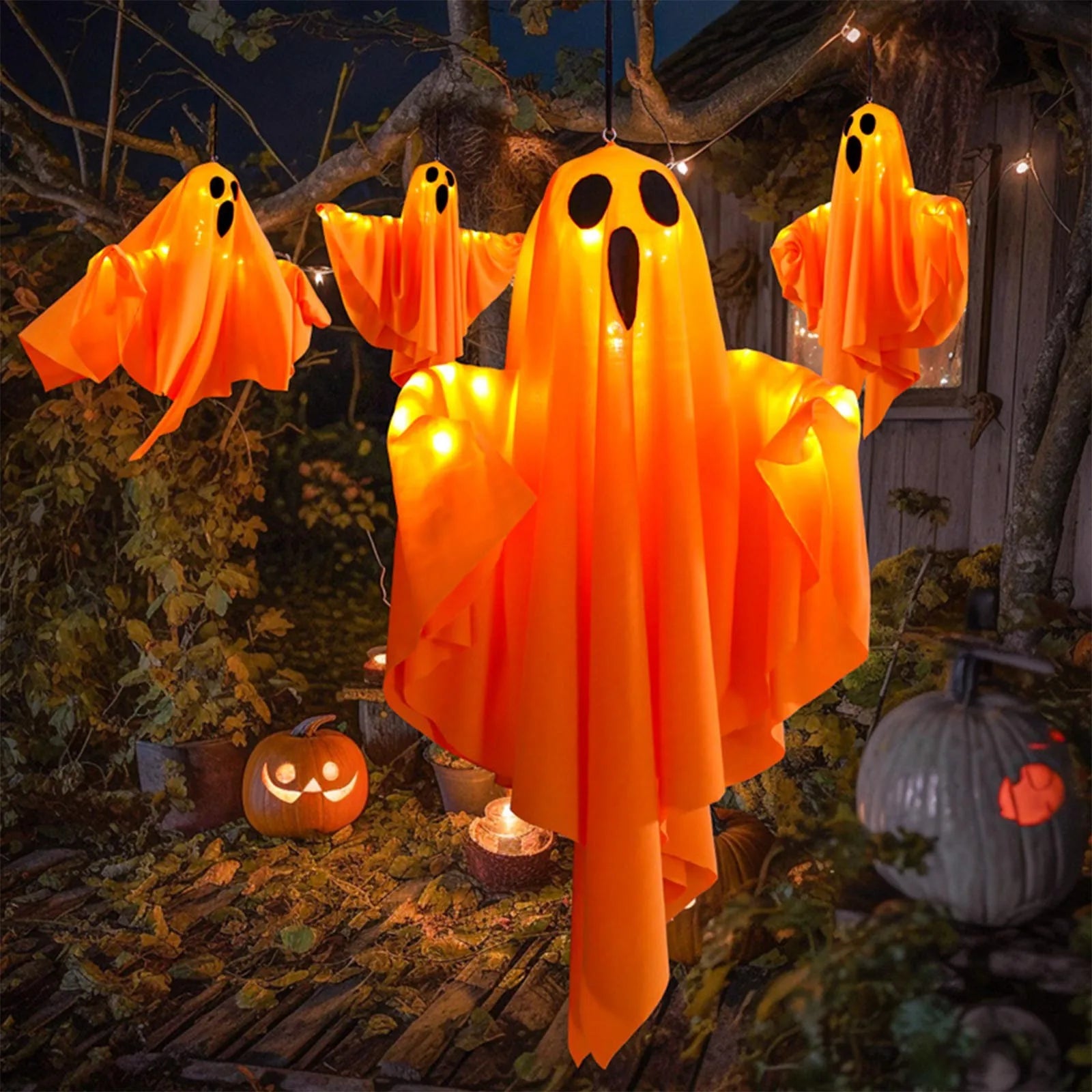Orange glowing fabric ghost hanging in a tree alongside three smaller ghosts at night
